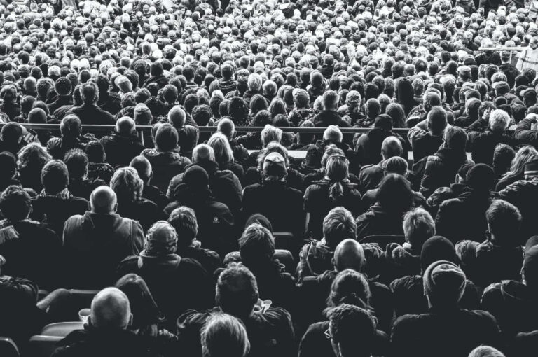 A monochrome image of a large audience taken from behind.