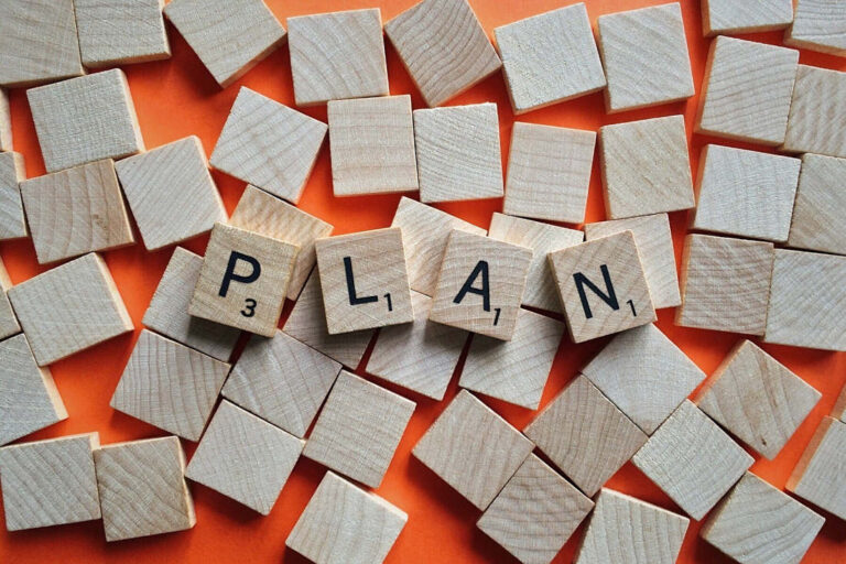 Pale square wooden blocks on an orange background. In the middle 4 scrabble-like blocks spell out 'PLAN'